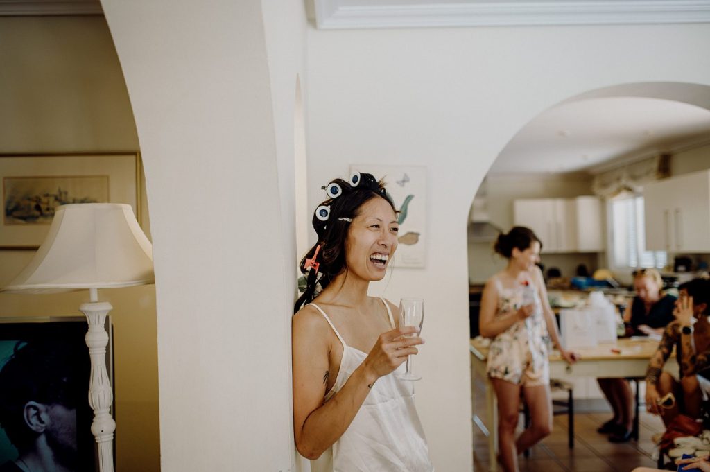 Mujer riendo con rulos, copa de champán en mano.